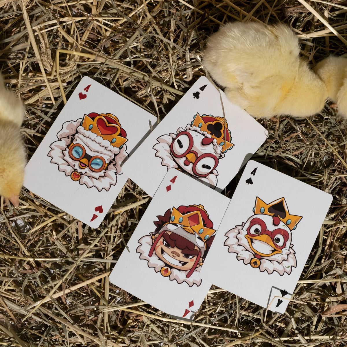 Four playing cards with cartoon chicken designs on a bed of straw.