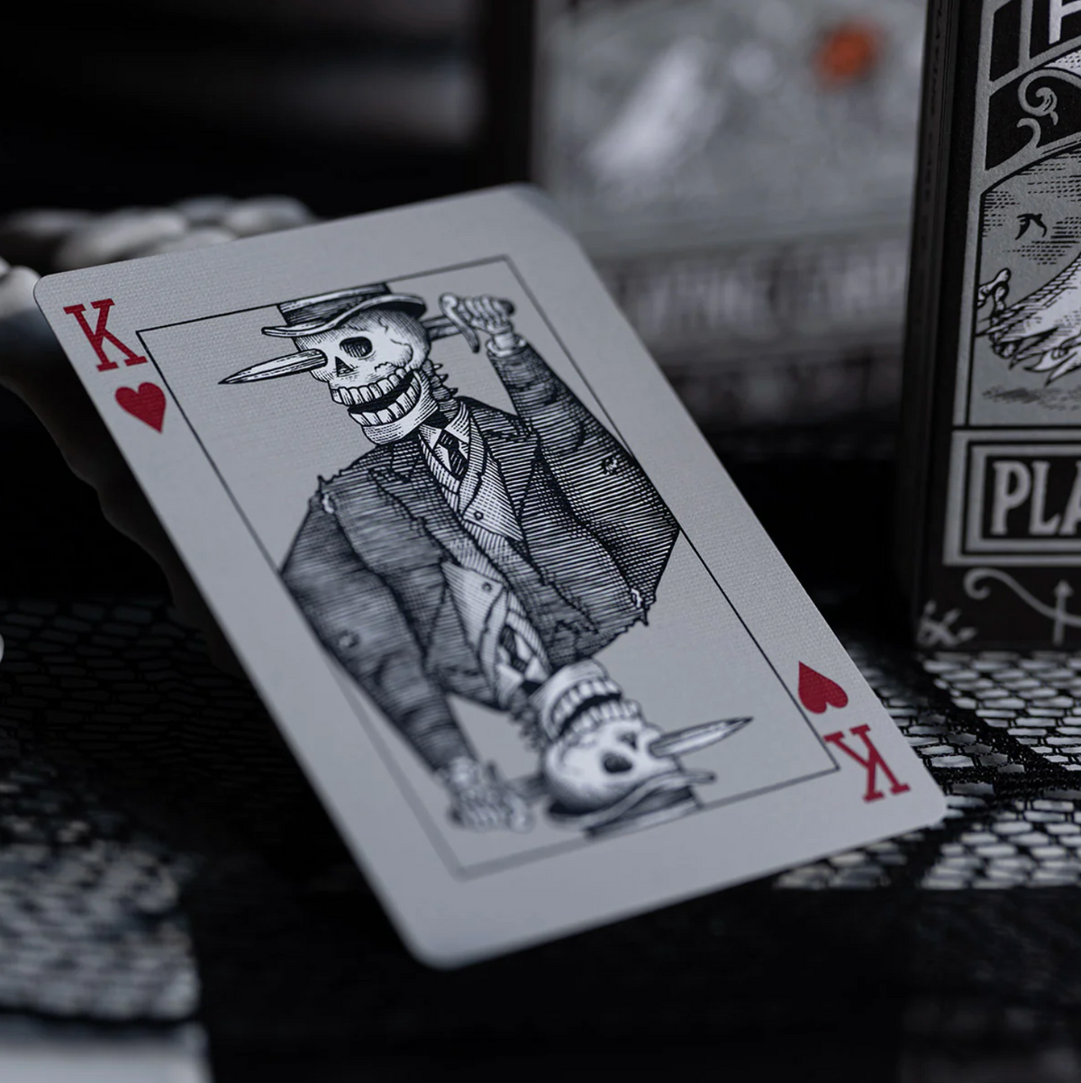 Playing card with a skeleton in a suit and top hat, next to a deck of cards.