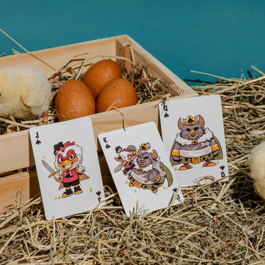 Three playing cards with cartoon characters on a wooden crate with oranges and hay, against a blue ocean background.