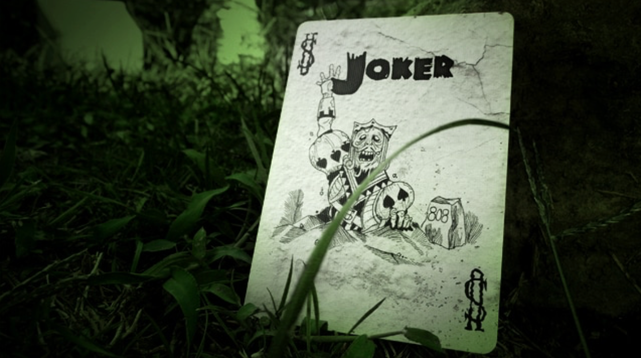Joker card lying on grass with a dark, eerie background