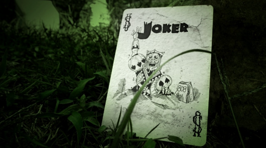 Joker card lying on grass with a dark, eerie background