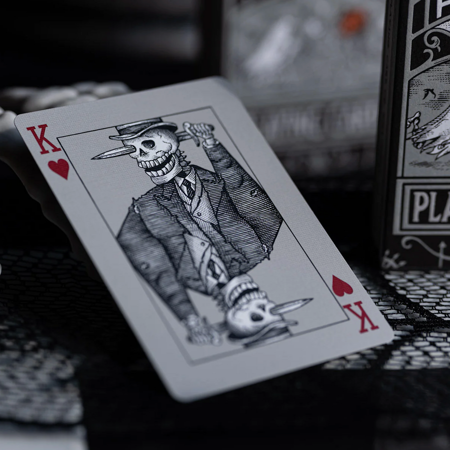 Playing card with a skeleton in a suit and top hat, next to a deck of cards.