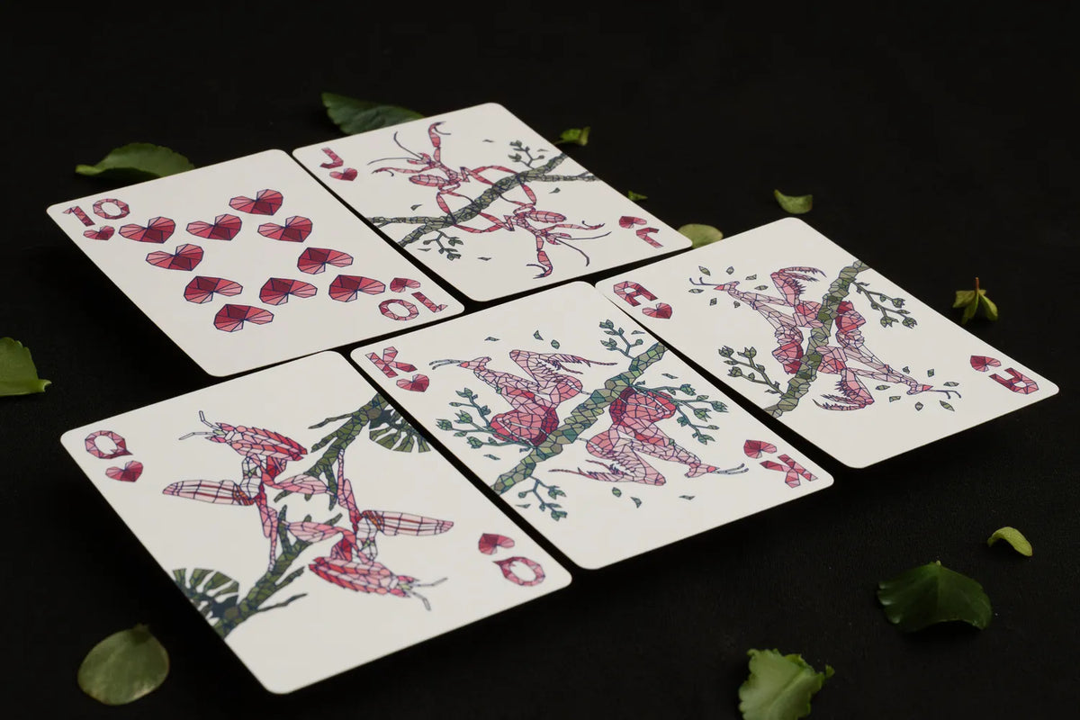 Five illustrated playing cards arranged on a black background with scattered green leaves. The cards feature red hearts and pink-and-red mantis with green branches on white card faces.