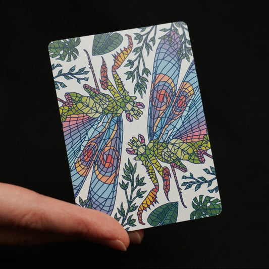 A hand holding a rectangular playing card featuring a colorful stained-glass Mantis design against a solid black background.