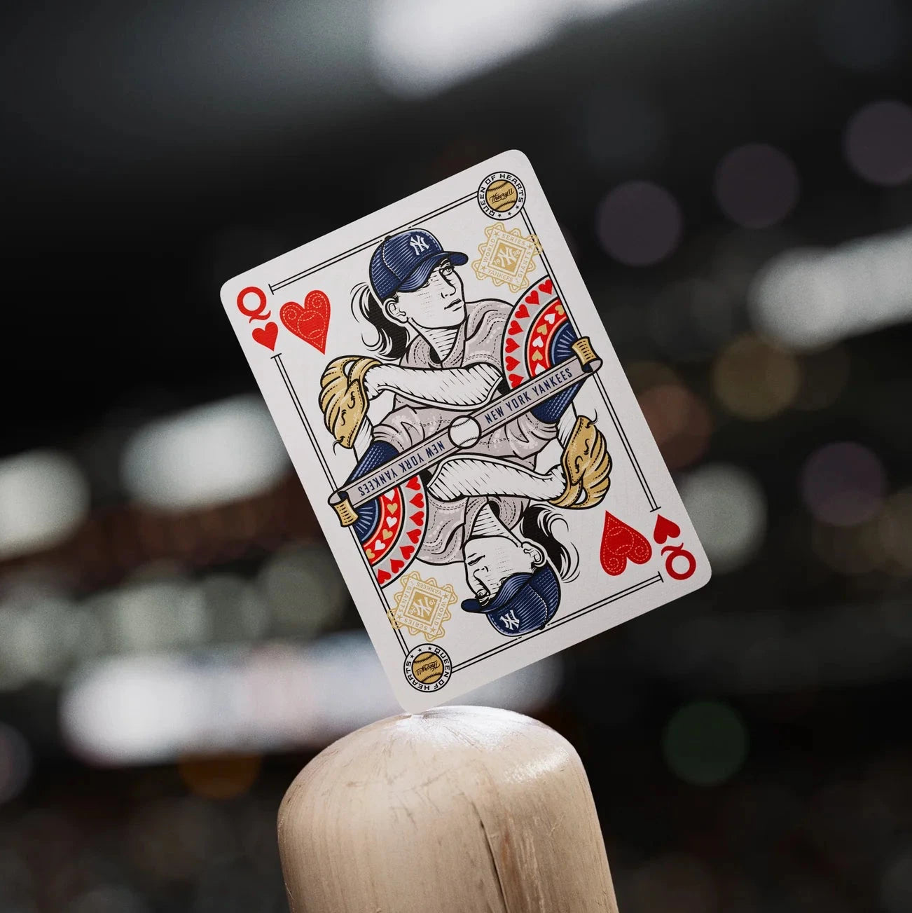 Queen of Hearts playing card held by a wooden stick against a blurred background