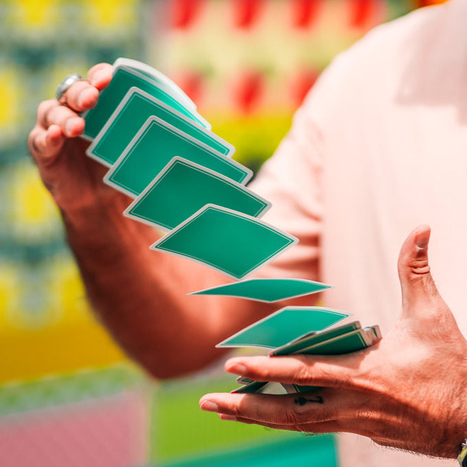 Person performing a card trick with green playing cards against a colorful background