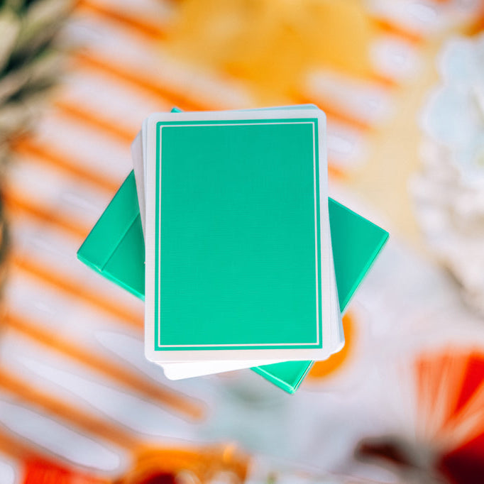 Green playing cards with a blurred colorful background featuring a pineapple and flowers.