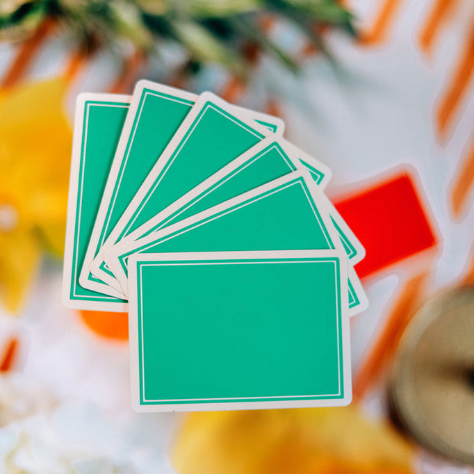 Stack of green playing cards on a decorative surface with flowers and a clock.