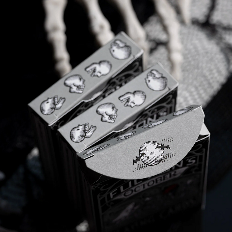 Playing cards with skull designs on the box, held by a person.
