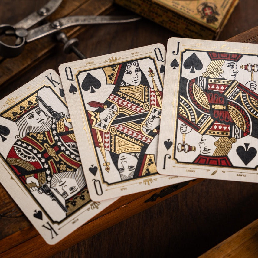 Three playing cards (King, Queen, Jack of Spades) on a wooden surface with vintage tools.