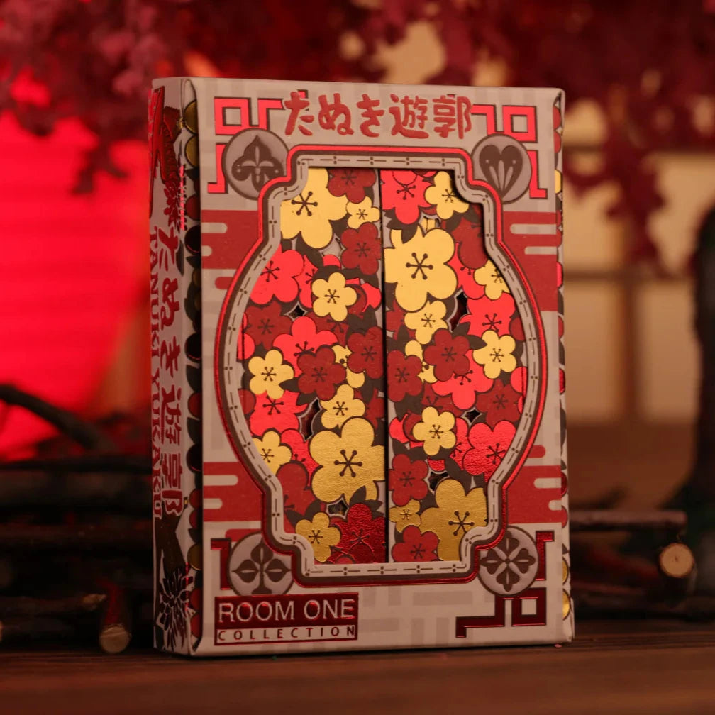 Playing card box with floral design and 'Room One' branding on a blurred background