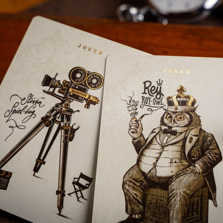 Playing cards with vintage-style illustrations of a camera and an owl in a suit on a wooden surface.