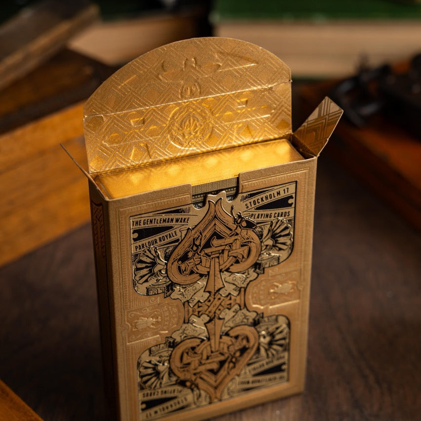 Gold playing card box with intricate designs on a wooden surface
